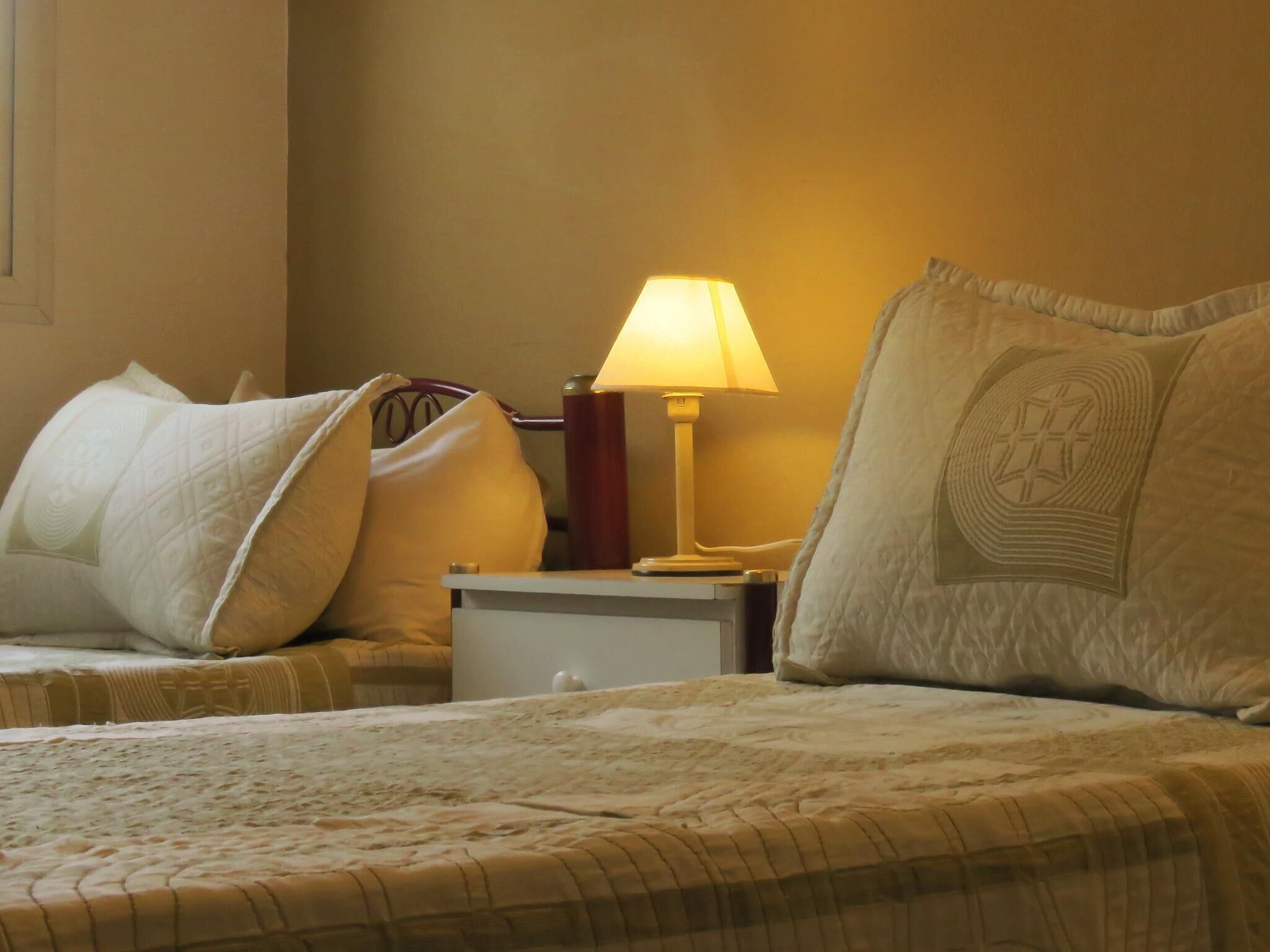 A hotel room with a bed, pillows, a nightstand, and a lamp.