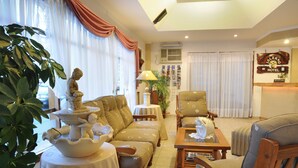 A hotel reception area with a sofa, armchairs, a small table with a lamp, and a decorative fountain. - Hotel Salerno (Villa Carlos Paz)