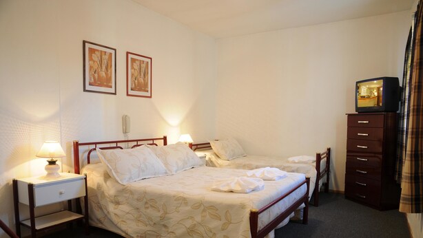 A bedroom with two single beds, a nightstand with a lamp, a dresser, and a television on top of the dresser. - Hotel Salerno (Villa Carlos Paz)