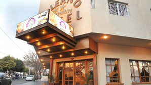 The exterior of the Verno Premium Hotel with illuminated signage, large windows, and potted plants at the entrance. - Hotel Salerno (Villa Carlos Paz)