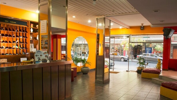 A hotel reception area with a wooden counter, a large mirror, and a glass door leading outside. - Hotel Castelmar (Mar del Plata)