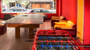 A foosball table, a sofa, and a table in a room with red walls and a view of the street outside. - Hotel Castelmar (Mar del Plata)