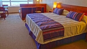 Habitación de hotel con una cama grande, un escritorio y una silla. Se ve una ventana con vistas al océano.