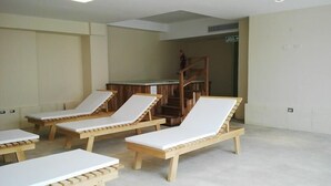 Una habitación con cuatro sillones de madera con cojines blancos, una mesa de madera y una escalera que sube a un nivel superior.