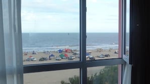 Vista de la playa a través de una ventana, con tiendas de campaña y coches en la arena.