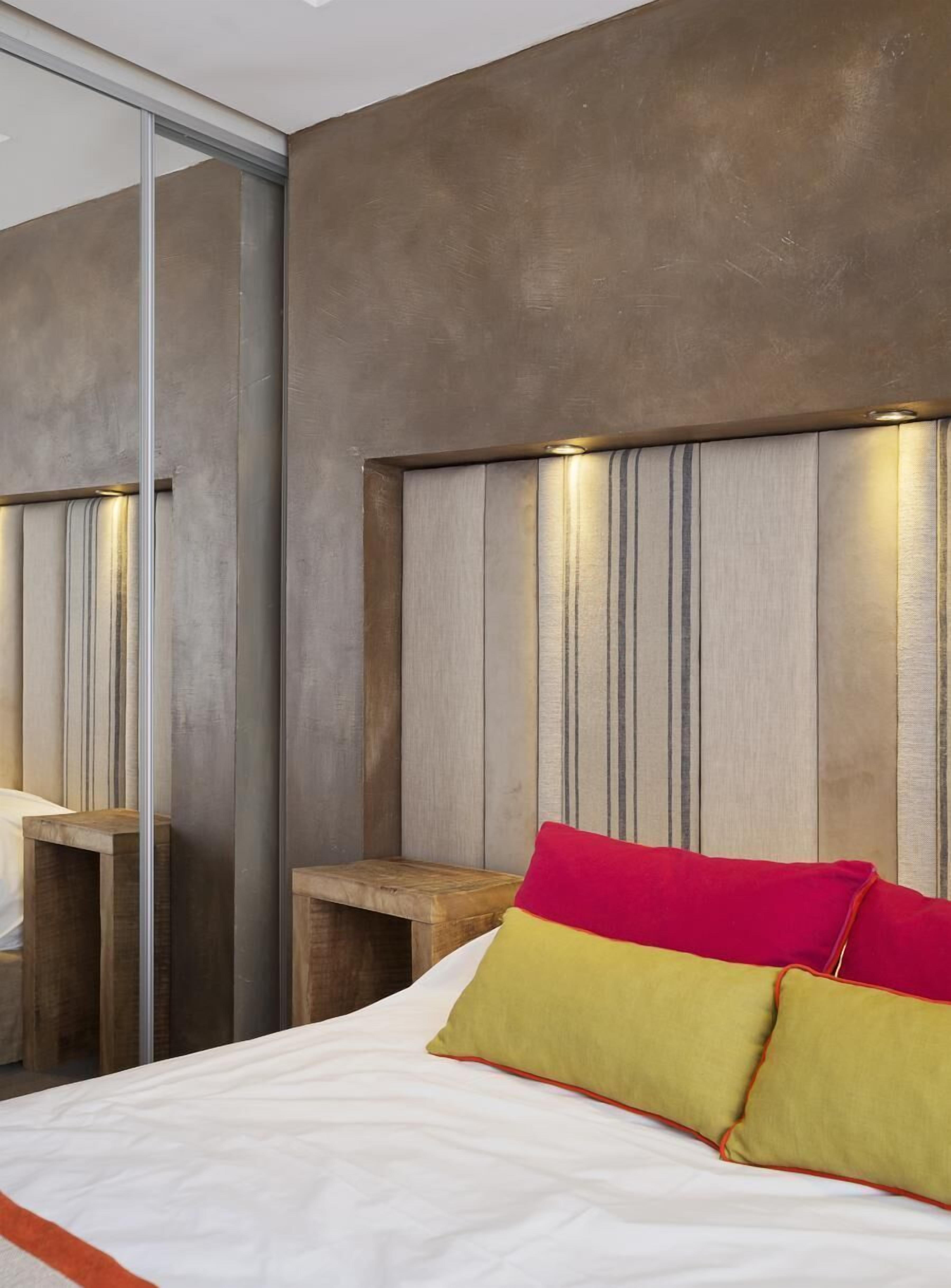 A modern bedroom with a large bed, wooden headboard, and a bedside table.