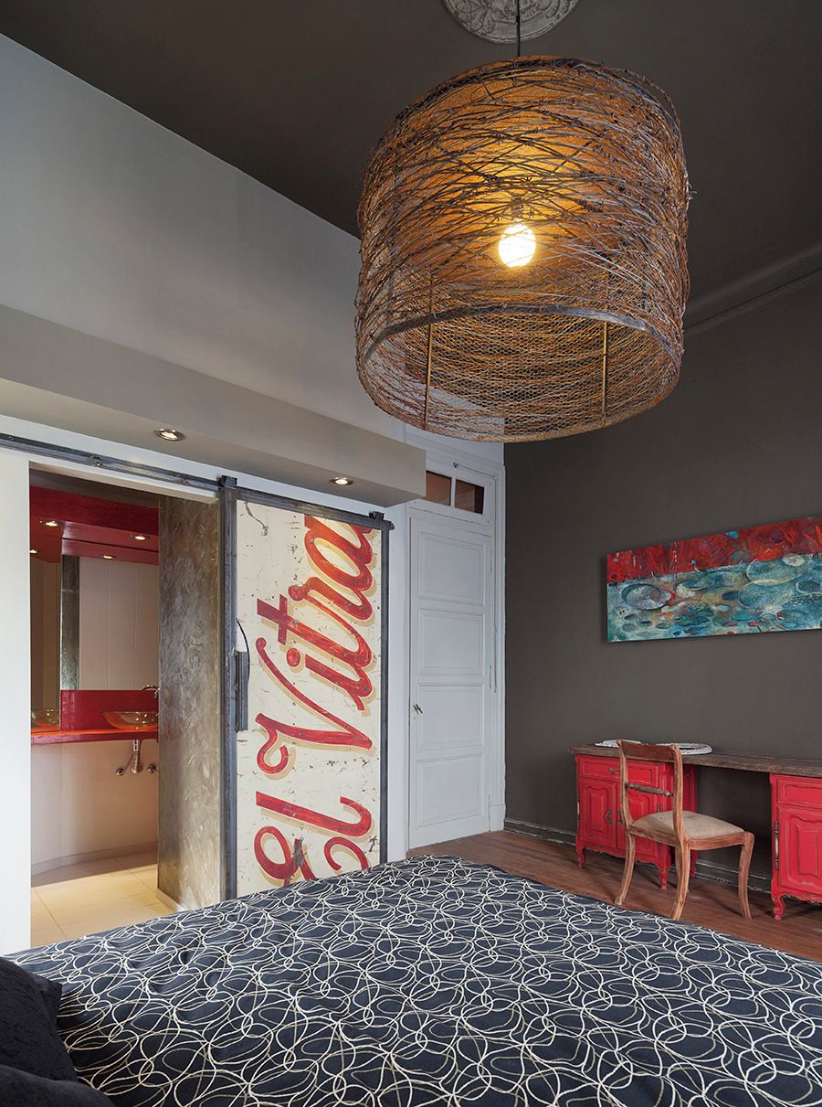 A bedroom with a bed, a hanging light fixture, a desk, and a chair.