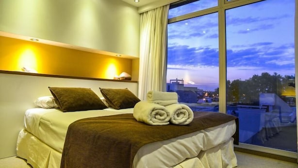 A hotel room with a large window, a bed with a brown headboard, and a nightstand with a lamp. - Ambit Boulevard Hotel Boutique (Santa Fe)