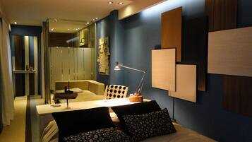 A modern bedroom with a bed, a desk, and a chair. There is a mirror, a lamp, and a wardrobe.