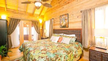 A wooden cabin room with a bed, ceiling fan, and a large window with curtains.