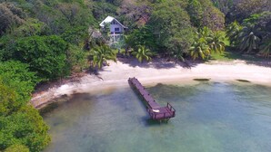 A coastal property with a wooden dock extending into clear waters, surrounded by lush greenery and a white house. - Casa de Rexanna upper (Roatan)