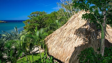 A thatched-roof structure surrounded by lush greenery and a clear blue sky.