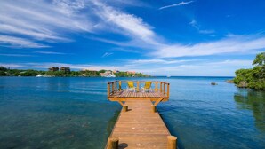 A wooden pier extending into a clear blue body of water with a wooden deck and two yellow chairs at the end. - Casa de Rexanna upper (Roatan)