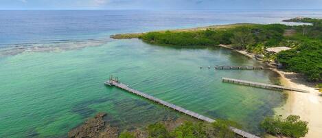 A coastal area with clear turquoise waters, a sandy beach, and a wooden pier extending into the sea.