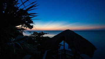A beach view with a thatched hut and wooden deck.