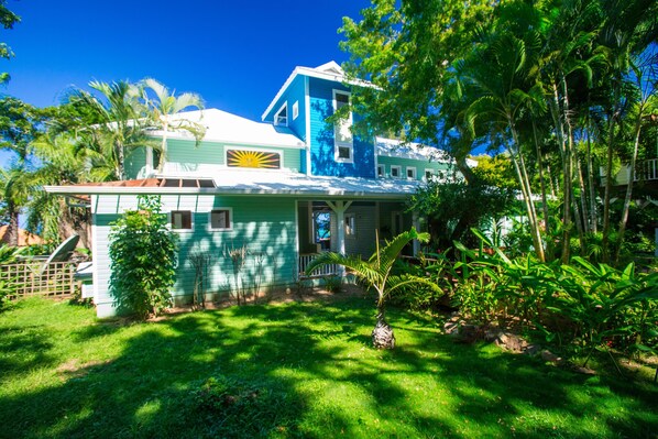 A two-story house with a blue and white exterior, a visible garage, and a lush garden with various plants and trees.