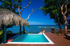 A wooden deck with a pool overlooking a beach and the ocean.