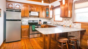 A kitchen with wooden cabinets, stainless steel appliances, a granite countertop, and wooden stools. - Casa Feliz (Roatan)