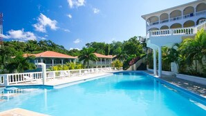 A swimming pool with a white fence and palm trees in the background. - Casa Feliz (Roatan)