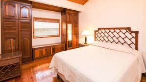 A bedroom with a wooden headboard, a wooden wardrobe, a bench, and a bedside table with a lamp. - Casa Feliz (Roatan)