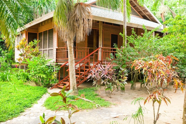 A wooden house with a porch and stairs, surrounded by lush greenery and plants. - Casa Flores (Roatan)