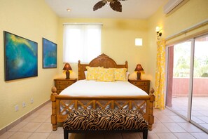 Un dormitorio con una cama de madera, dos mesitas de noche con lámparas, un banco estampado con diseño de cebra y dos cuadros abstractos en la pared.