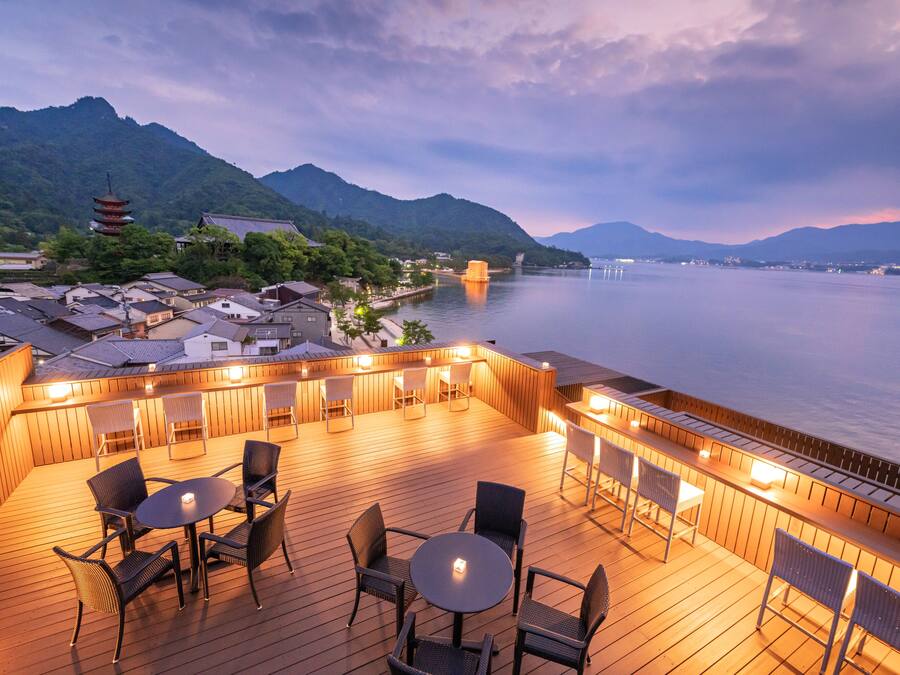 Una terraza de madera con mobiliario exterior y vistas a una montaña y al agua.