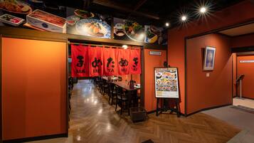 A restaurant interior with wooden floors, red banners, and a menu stand.