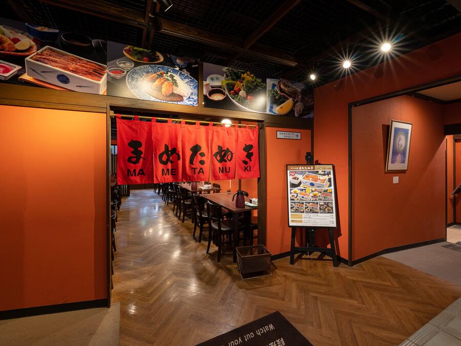 A restaurant interior with wooden floors, red banners, and a menu stand.