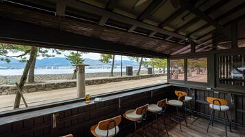 A restaurant with outdoor seating, a view of the beach, and mountains in the background.
