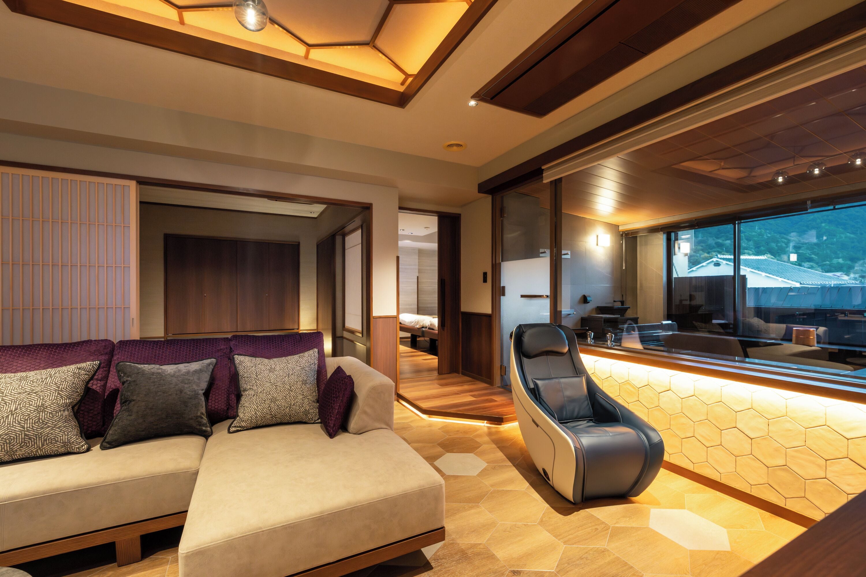 Un espacio de sala moderno con un sofá, un sillón de masaje y vistas al exterior a través de amplios ventanales.