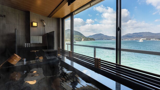 A modern spa with a large glass window overlooking a body of water and mountains. - Miyajima Kinsuikan (Hatsukaichi)