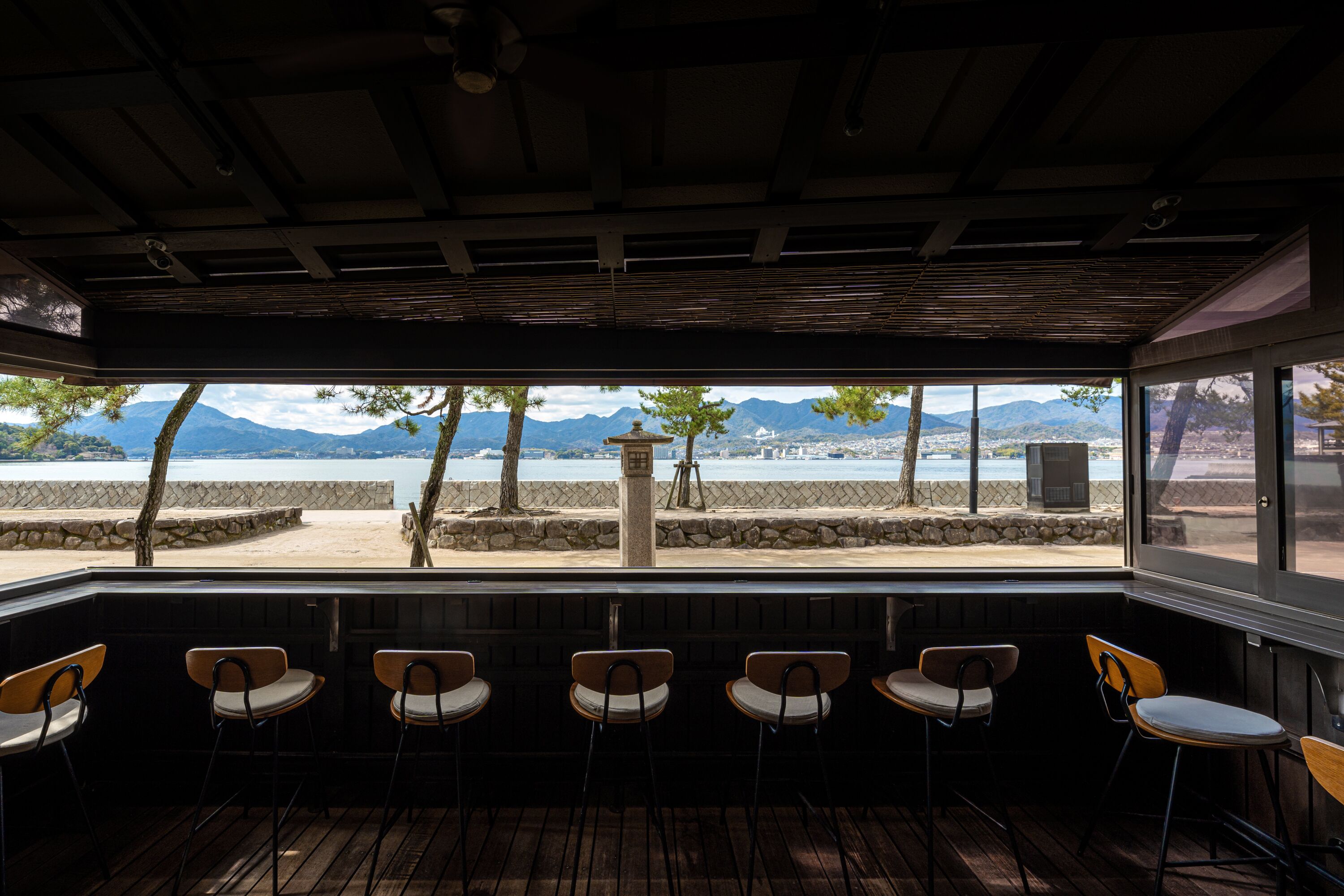 Un área de estar al aire libre con sillas de madera y vistas a la playa y montañas.