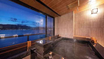 A modern spa with a large hot tub, wooden paneling, and a view of a cityscape at dusk.