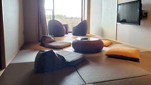 A modern room with a large window, a flat-screen TV, and a seating area with cushions and a small table.