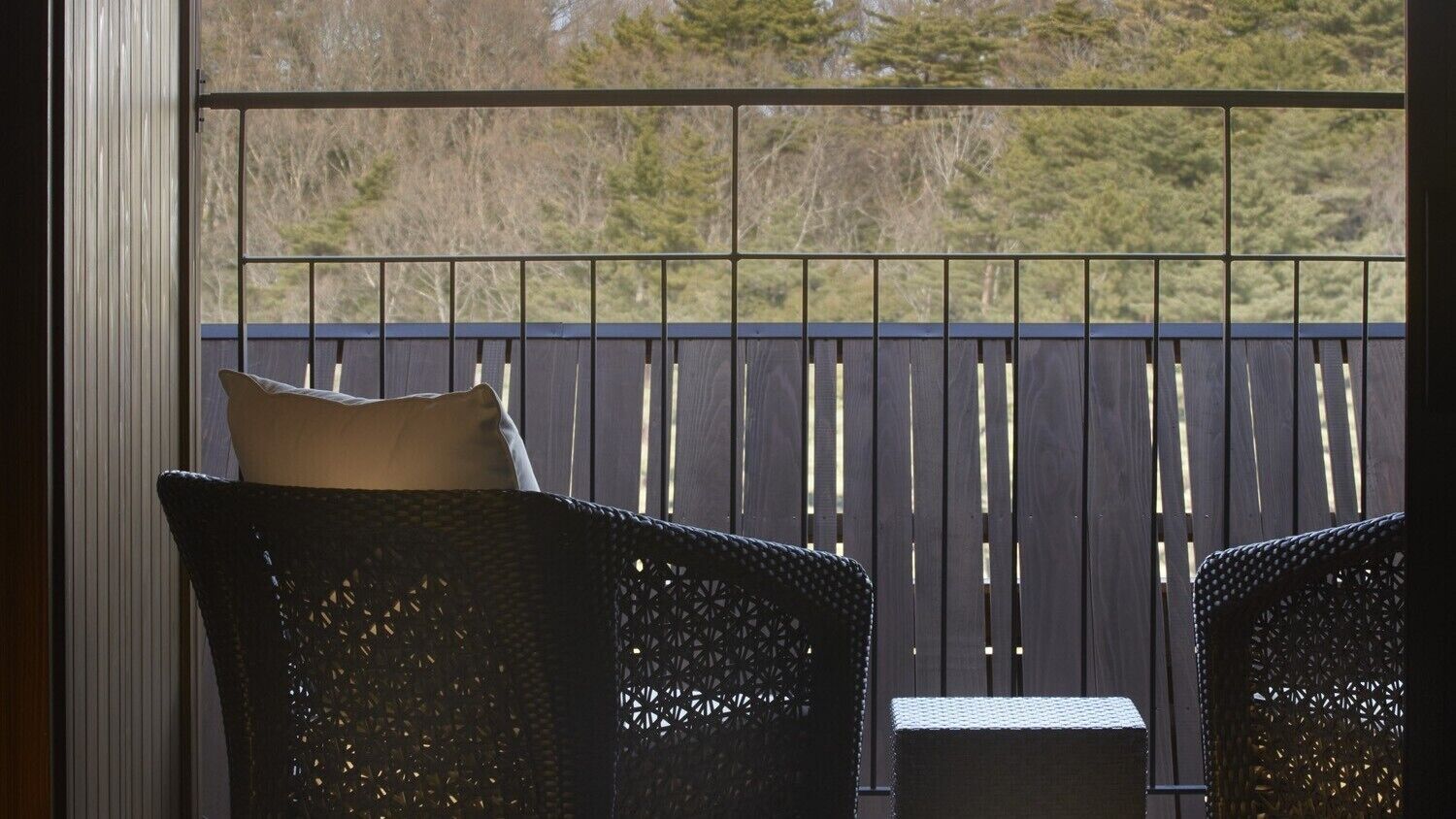 Un balcon avec deux fauteuils en osier et une petite table, donnant sur une terrasse en bois et des arbres.
