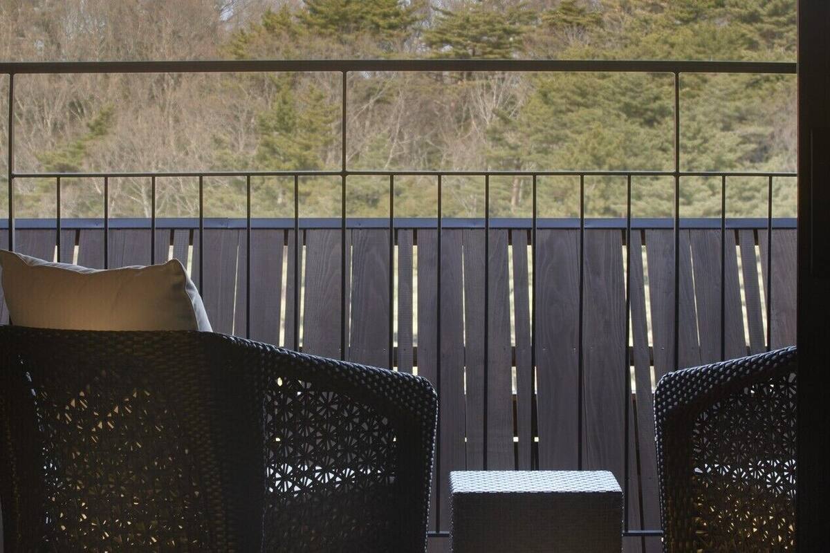 Ein Balkon mit zwei Korbstühlen und einem kleinen Tisch, mit Blick auf eine Holzterrasse und Bäume.