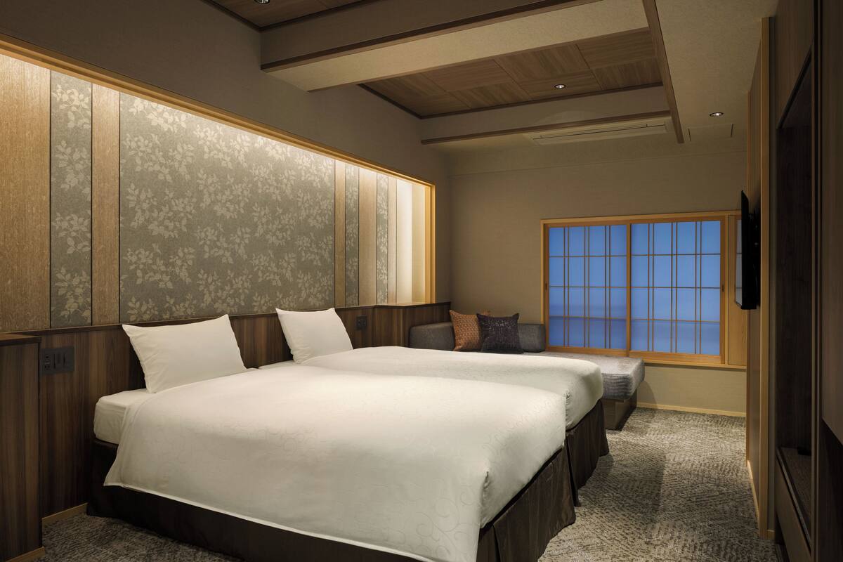 Ein Hotelzimmer mit zwei Betten, einem großen Fenster und einer Holzbalkendecke.