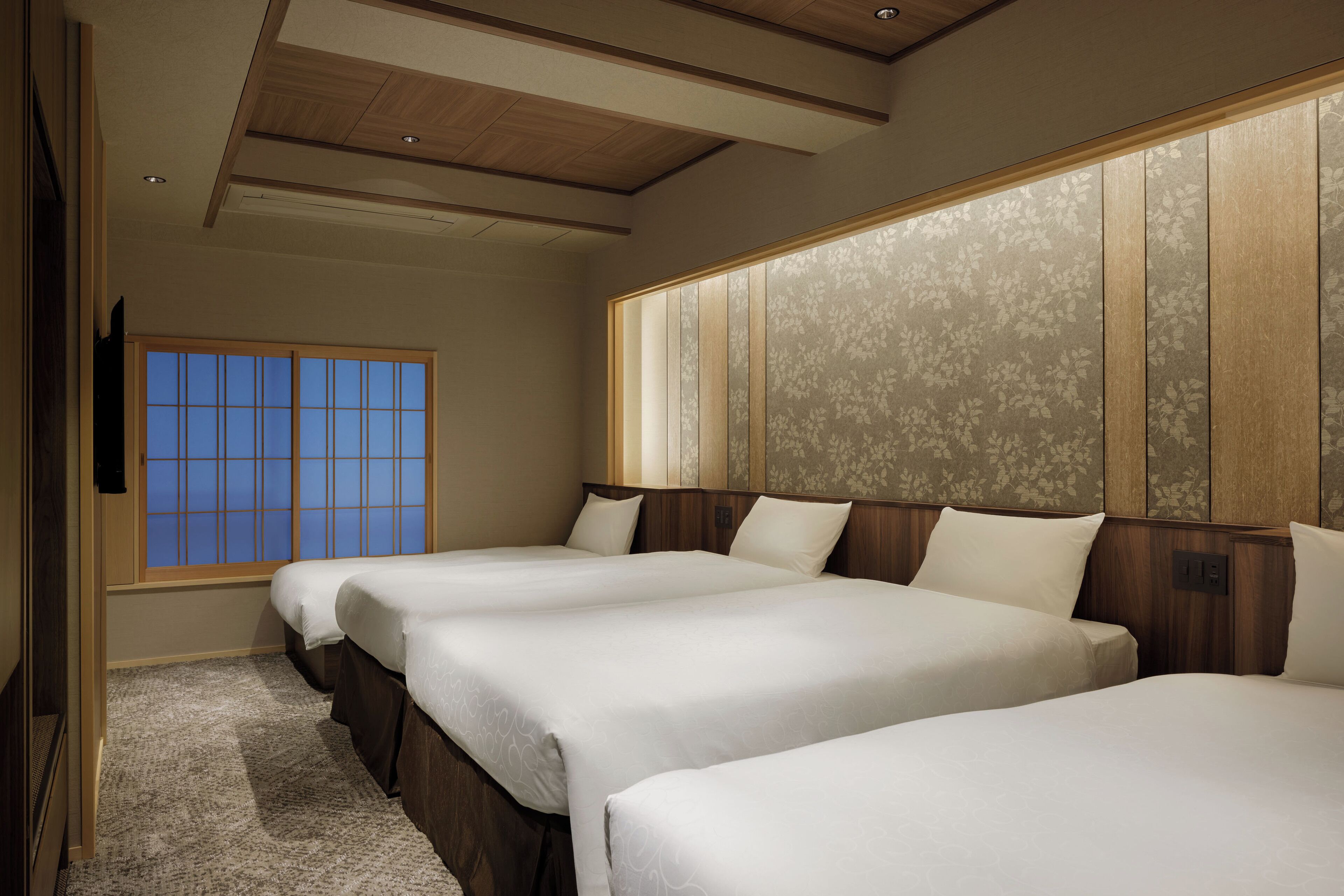 A hotel room with two beds, a large window, and a wooden ceiling.