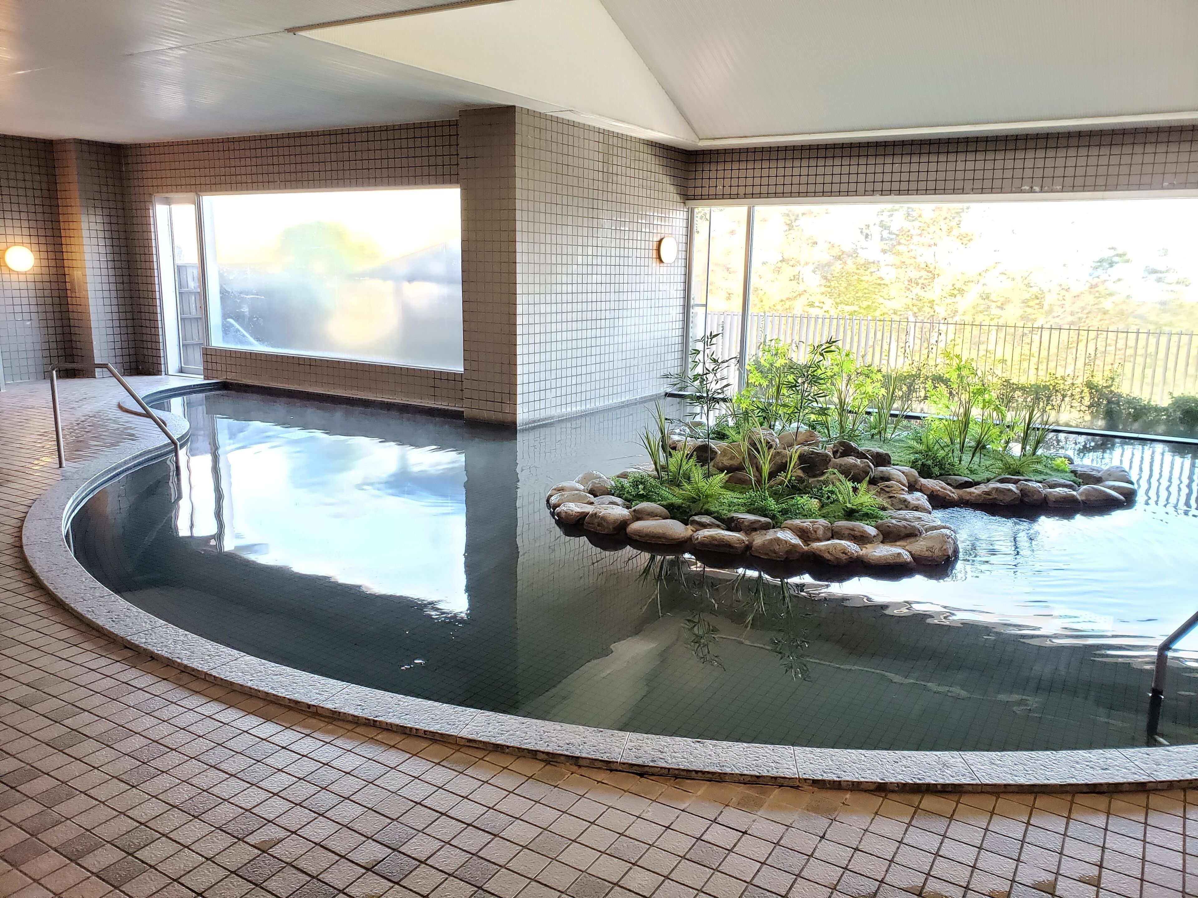 Una piscina de diseño circular, rodeada por un solárium con baldosas y un pequeño jardín de rocas.