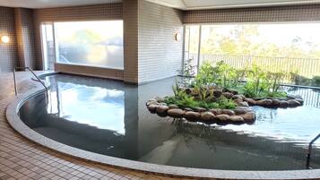Una piscina de diseño circular, rodeada por un solárium con baldosas y un pequeño jardín de rocas.