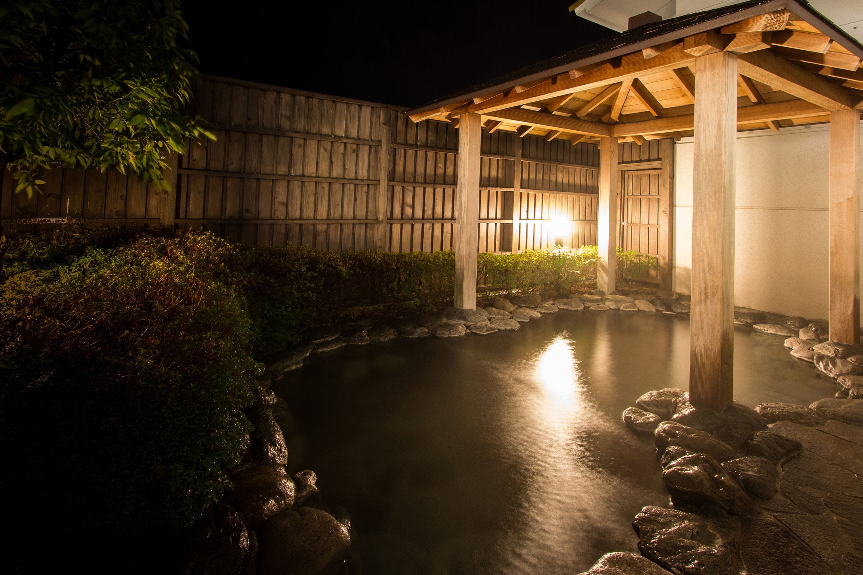 A tranquil outdoor area with a wooden pergola, a stone pathway, and a water feature.