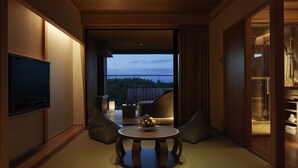 A room with a television, a round table with a flower centerpiece, and a view of the outdoors.