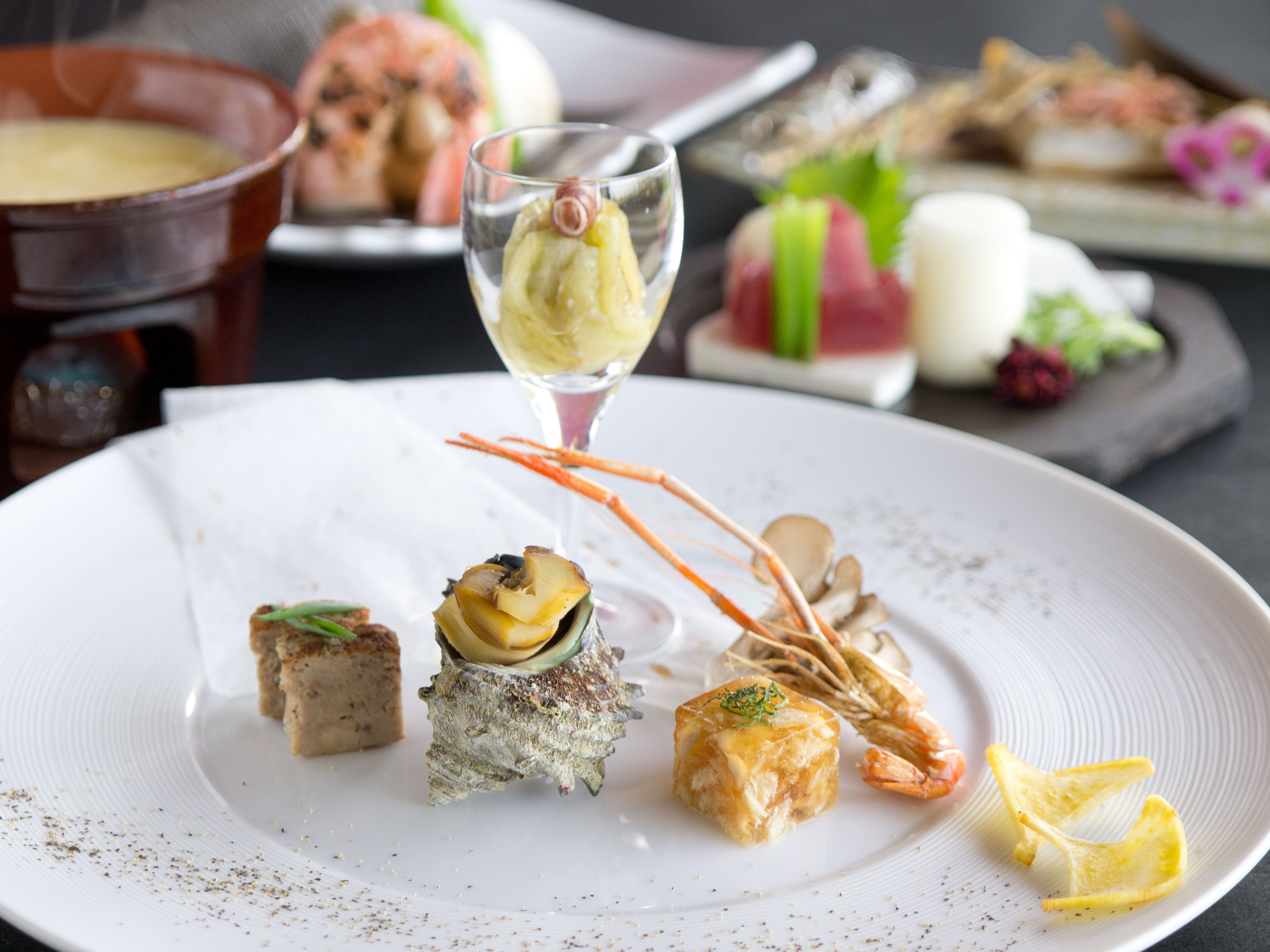 A variety of gourmet dishes on a white plate, including seafood and a glass of dessert.