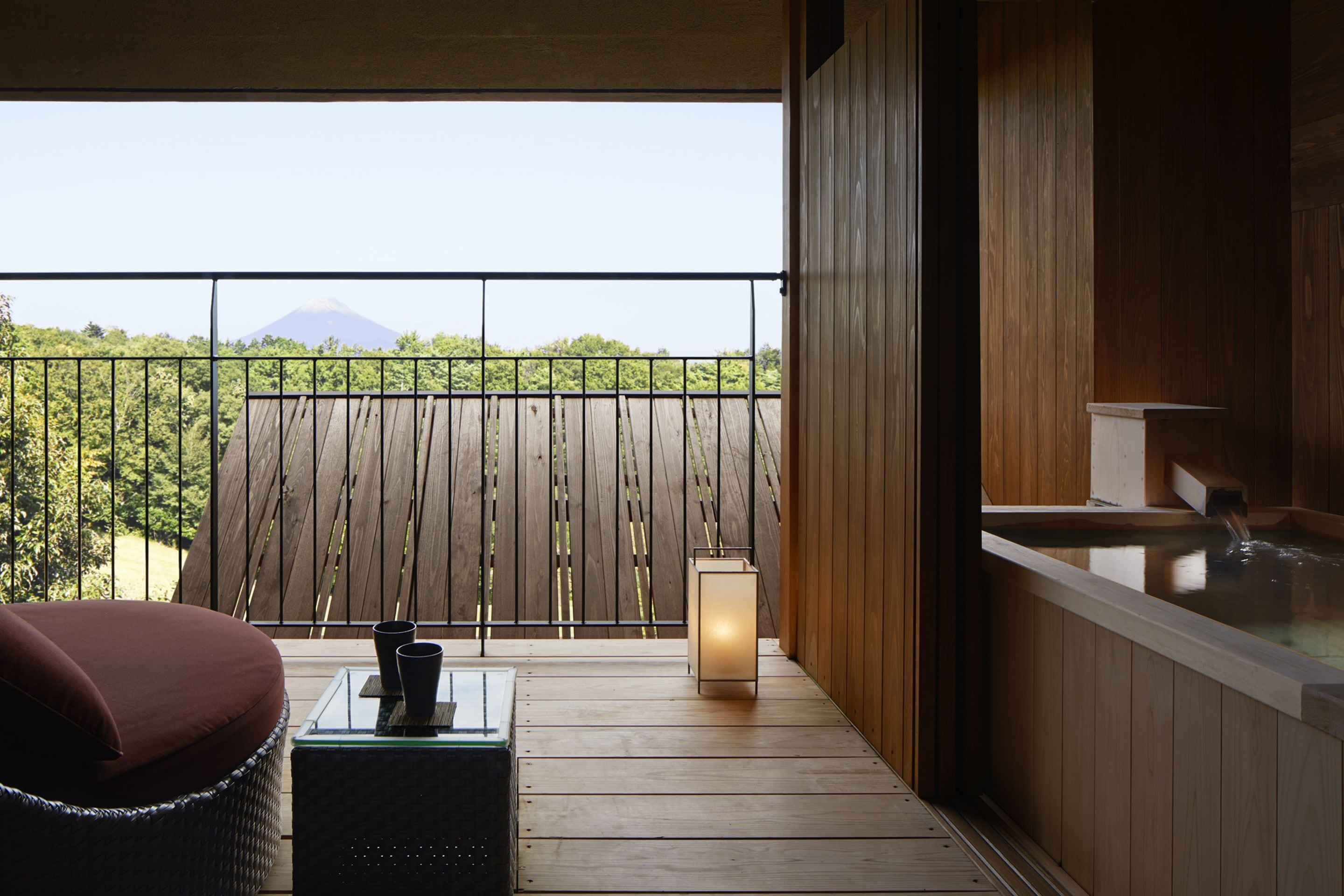 A balcony with a wooden floor, a cushioned chair, a table with a candle, and a hot tub.