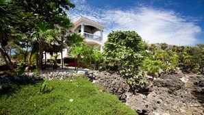 A building with a balcony, surrounded by lush greenery and rocky terrain.