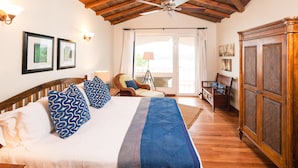 A bedroom with a large bed, wooden headboard, and a ceiling fan. There is a window with curtains, a wooden cabinet, and a chair with a cushion. - Coral Vista 4 3 bedroom option (Roatan)