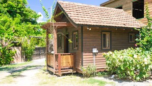 A wooden cabin with a tiled roof, a porch, and a garden. - Green Bamboo Cabana (Roatan)
