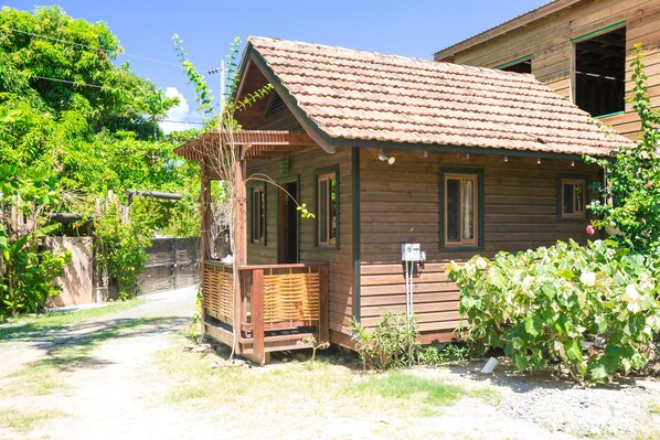 A wooden cabin with a tiled roof, a porch, and a garden.