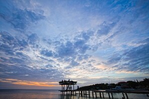 A pier extending into calm waters with a wooden structure at the end, surrounded by trees and buildings.